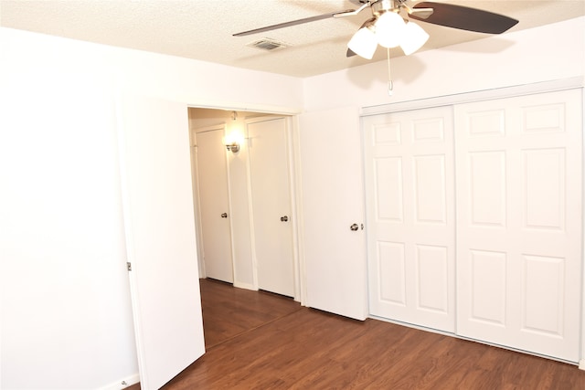 unfurnished bedroom featuring a textured ceiling, dark wood-type flooring, ceiling fan, and a closet