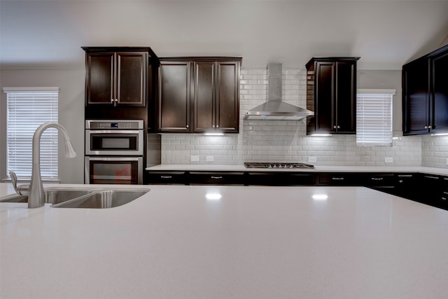 kitchen with stainless steel appliances, wall chimney exhaust hood, decorative backsplash, and sink