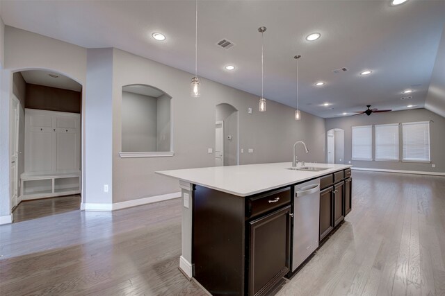 kitchen with sink, an island with sink, stainless steel dishwasher, pendant lighting, and light hardwood / wood-style flooring