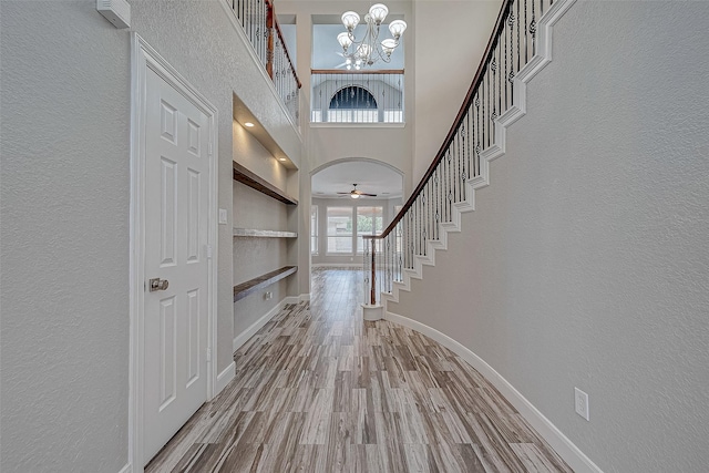 entryway with ceiling fan with notable chandelier, wood-type flooring, and a towering ceiling