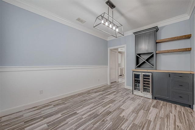 bar featuring ornamental molding, beverage cooler, pendant lighting, light hardwood / wood-style flooring, and gray cabinets