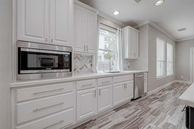 kitchen featuring decorative backsplash, appliances with stainless steel finishes, ornamental molding, sink, and white cabinetry