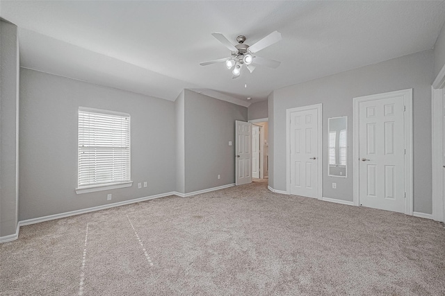 unfurnished bedroom with ceiling fan, light carpet, and two closets