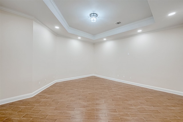 spare room with a raised ceiling, light wood-type flooring, and ornamental molding