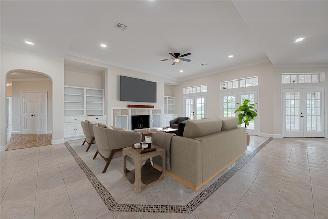 tiled living room with ceiling fan, ornamental molding, built in shelves, and french doors