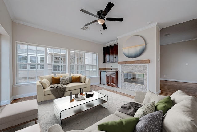 living room featuring light wood-type flooring, ornamental molding, ceiling fan, sink, and a fireplace