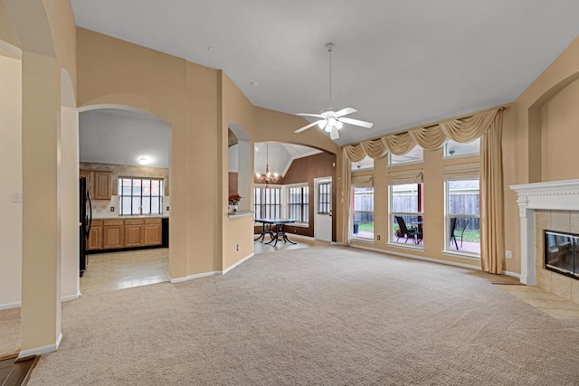 unfurnished living room with sink, light carpet, ceiling fan with notable chandelier, a tile fireplace, and vaulted ceiling