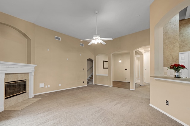 unfurnished living room featuring a tiled fireplace, light colored carpet, and ceiling fan