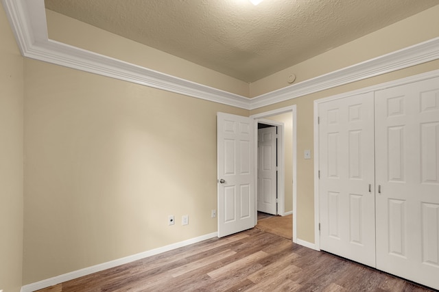 unfurnished bedroom featuring a closet, wood-type flooring, ornamental molding, and a textured ceiling