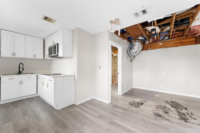 213 Super St, Houston, TX 77011 - kitchen with stainless steel microwave, light wood-type flooring, a sink, and white cabinets