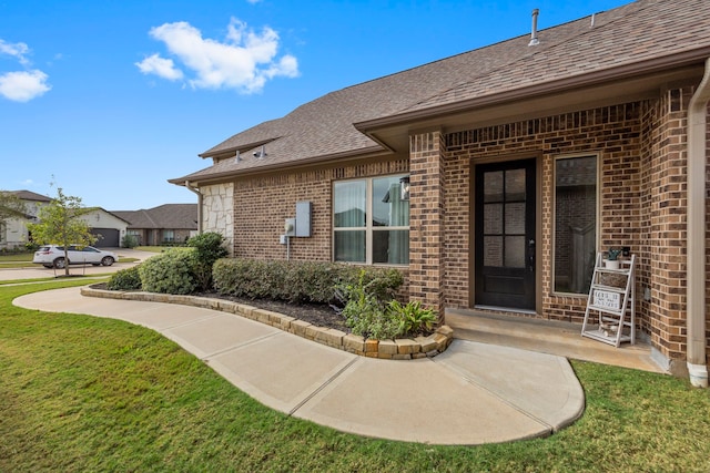 2215 Rose Manor Ct, Richmond, TX 77469 - view of exterior entry featuring brick siding, a shingled roof, and a yard