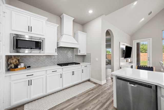 kitchen featuring custom exhaust hood, lofted ceiling, backsplash, white cabinetry, and stainless steel appliances