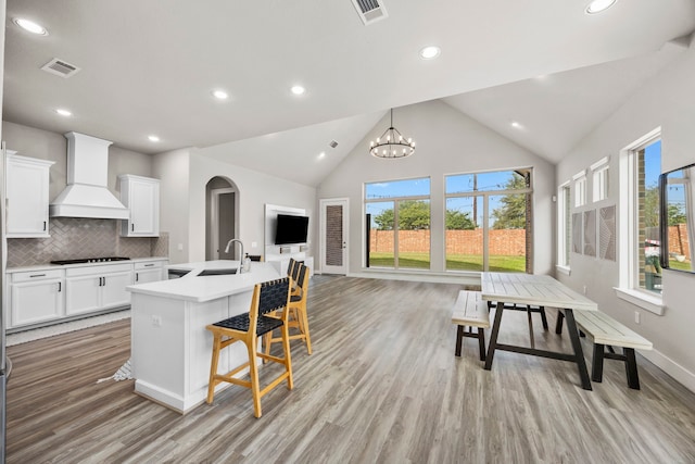 kitchen with premium range hood, an inviting chandelier, a center island with sink, tasteful backsplash, and white cabinetry