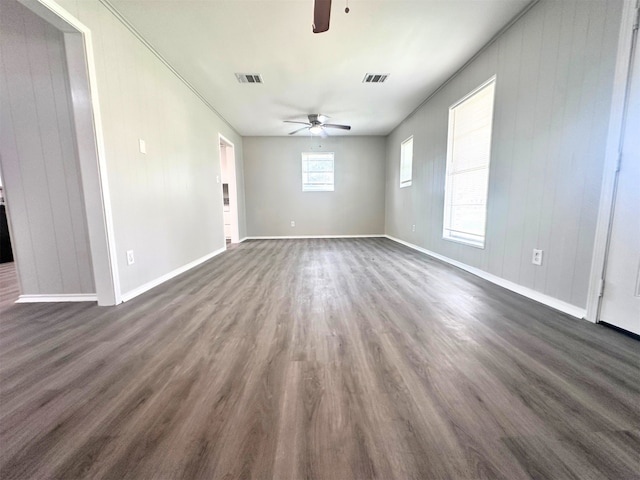 empty room with wood walls, ceiling fan, a wealth of natural light, and dark hardwood / wood-style floors