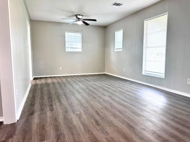 empty room featuring dark wood-type flooring, wood walls, and ceiling fan