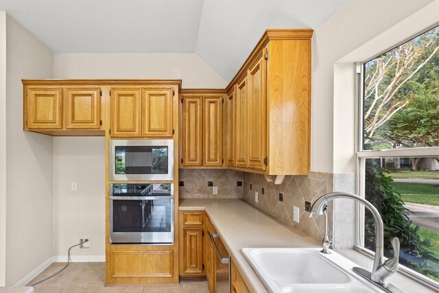 kitchen featuring sink, tasteful backsplash, lofted ceiling, light tile patterned floors, and appliances with stainless steel finishes