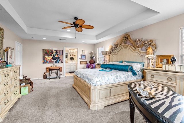 bedroom with ensuite bath, light carpet, and a raised ceiling