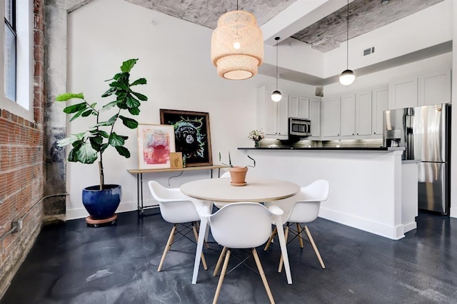 dining room with finished concrete flooring, visible vents, a high ceiling, brick wall, and baseboards