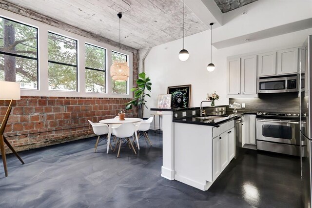 kitchen featuring stainless steel appliances, dark countertops, brick wall, concrete floors, and a peninsula