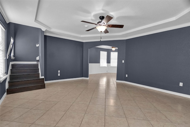 tiled empty room featuring ornamental molding, a tray ceiling, and ceiling fan