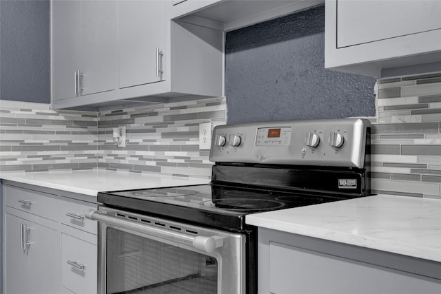 kitchen featuring tasteful backsplash, light stone countertops, and stainless steel electric stove