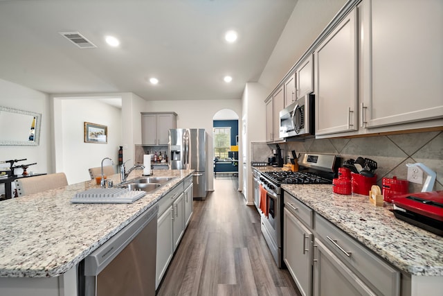 kitchen with backsplash, appliances with stainless steel finishes, gray cabinets, hardwood / wood-style flooring, and a kitchen island with sink