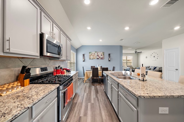 kitchen with stainless steel appliances, a center island with sink, sink, tasteful backsplash, and light hardwood / wood-style flooring