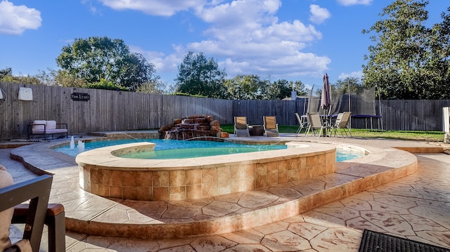 view of swimming pool featuring pool water feature, a patio, a hot tub, and a trampoline