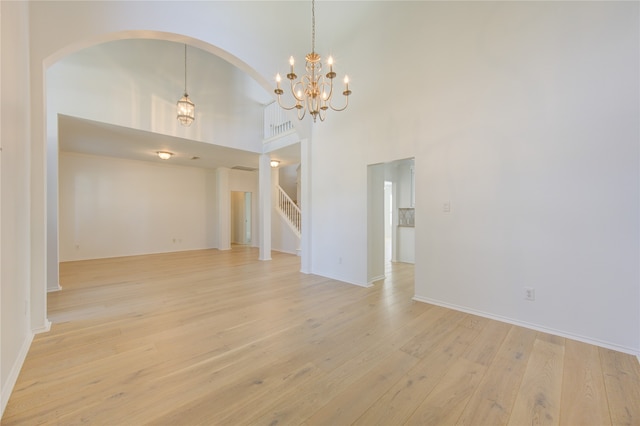 spare room with light hardwood / wood-style flooring, an inviting chandelier, and a towering ceiling