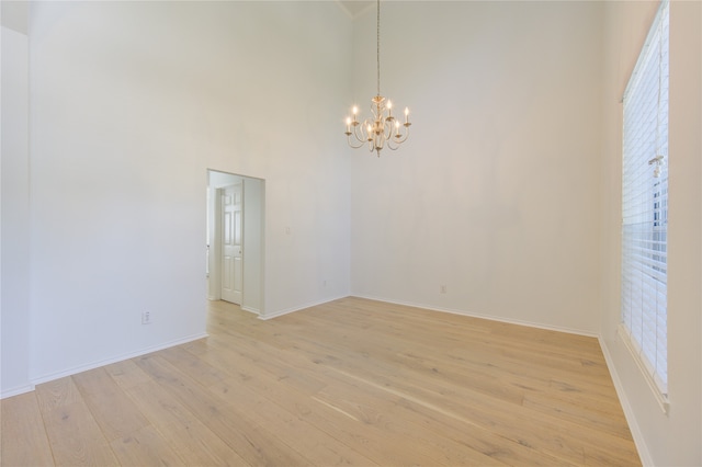 empty room featuring a towering ceiling, light hardwood / wood-style floors, and a chandelier