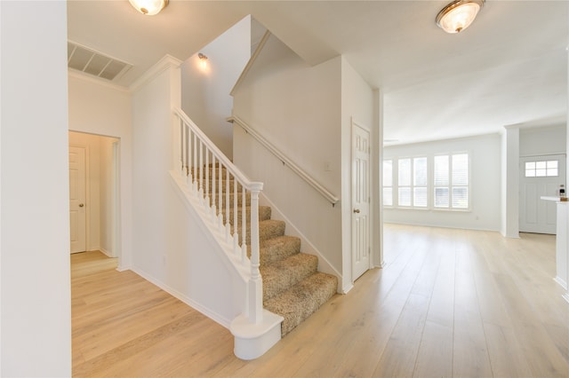 staircase with wood-type flooring and crown molding