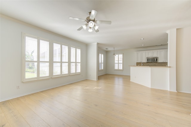 unfurnished living room featuring ceiling fan, a wealth of natural light, and light hardwood / wood-style floors