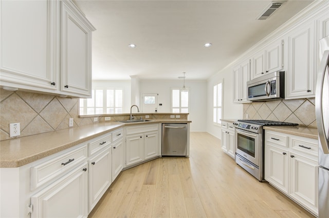 kitchen with stainless steel appliances, decorative light fixtures, sink, light hardwood / wood-style floors, and white cabinets