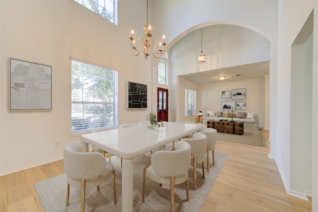 dining room featuring a towering ceiling, light wood-type flooring, and a notable chandelier