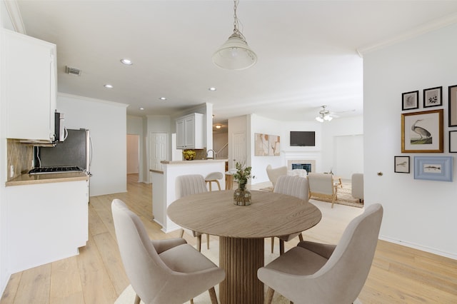 dining space with ceiling fan, sink, ornamental molding, and light hardwood / wood-style flooring