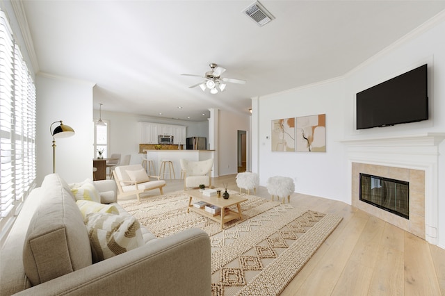 living room featuring light hardwood / wood-style floors, ceiling fan, a tile fireplace, and crown molding