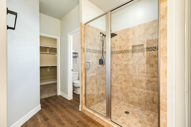 bathroom with hardwood / wood-style floors, a shower with shower door, and toilet