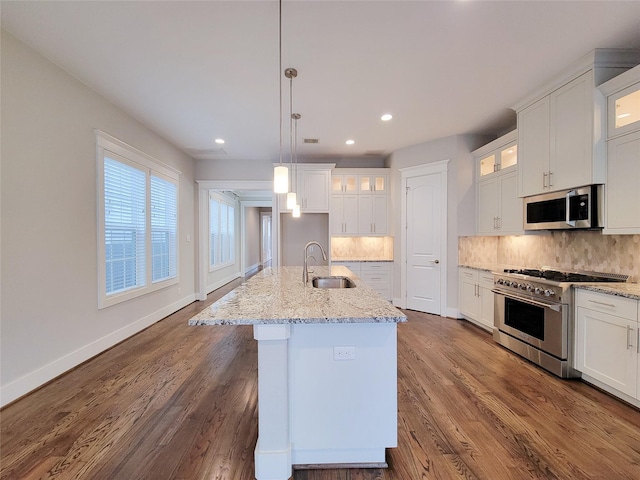 kitchen featuring sink, hanging light fixtures, stainless steel appliances, white cabinets, and a center island with sink