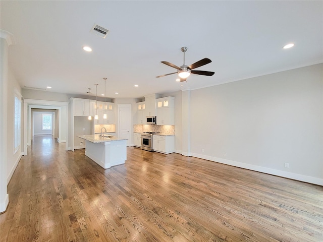 kitchen with pendant lighting, sink, white cabinetry, stainless steel appliances, and a center island with sink