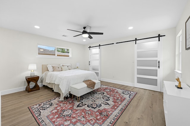 bedroom featuring a barn door, light hardwood / wood-style floors, and ceiling fan