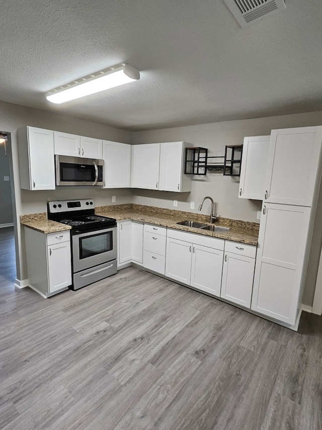 kitchen with stainless steel appliances, light wood-type flooring, white cabinetry, a textured ceiling, and sink