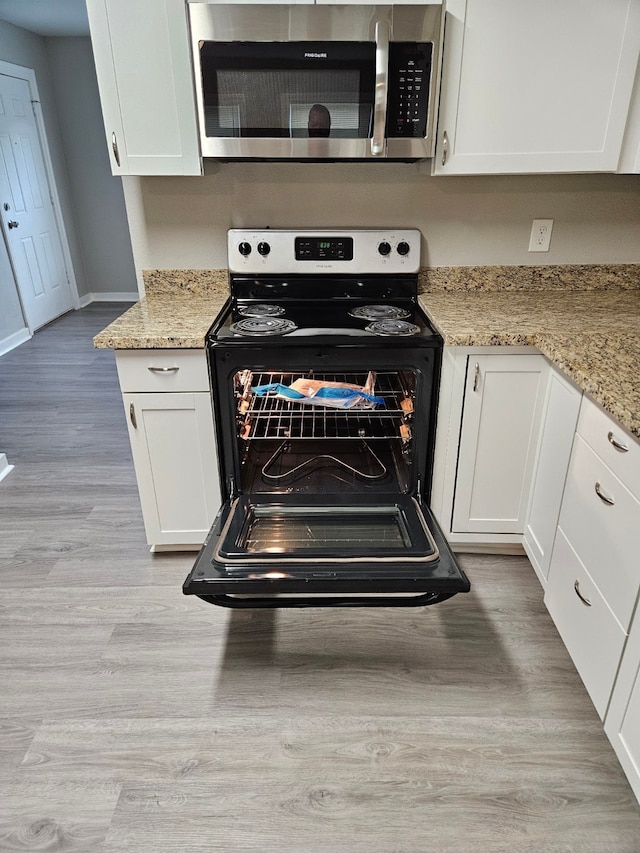 kitchen featuring light wood-type flooring, light stone counters, black electric range oven, and white cabinets