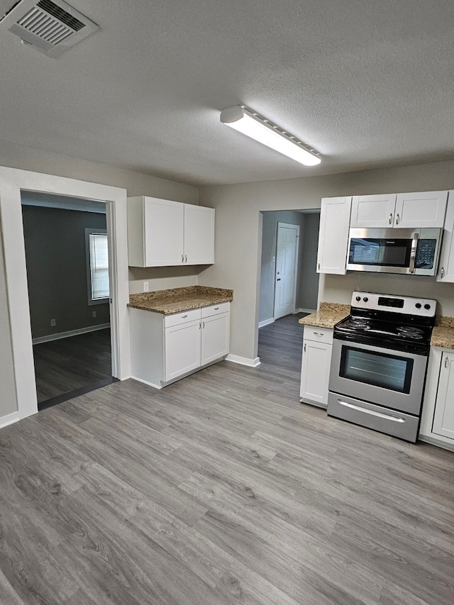 kitchen with white cabinets, light wood-type flooring, stainless steel appliances, and a textured ceiling