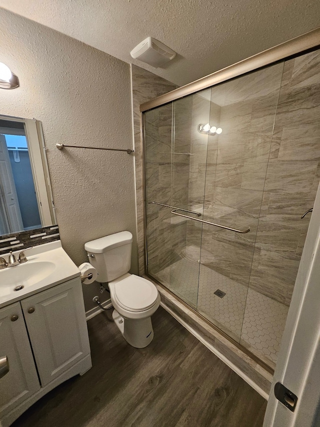 bathroom featuring wood-type flooring, a shower with door, vanity, a textured ceiling, and toilet