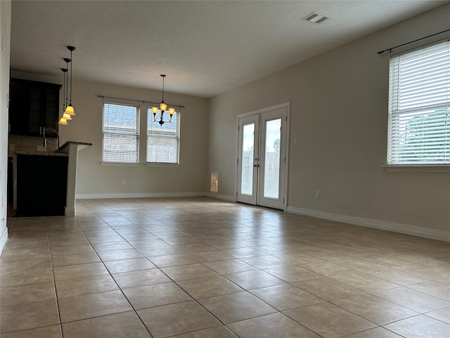 empty room with an inviting chandelier, a healthy amount of sunlight, and light tile patterned flooring