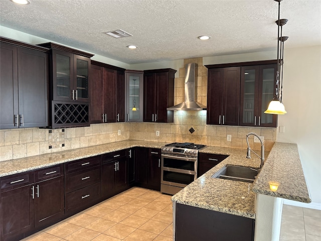 kitchen featuring kitchen peninsula, sink, wall chimney range hood, decorative light fixtures, and range with two ovens