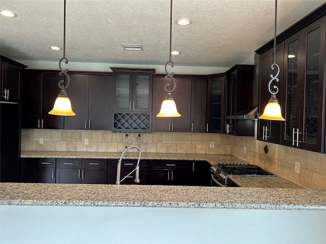 kitchen featuring sink, tasteful backsplash, stainless steel stove, decorative light fixtures, and dark brown cabinetry