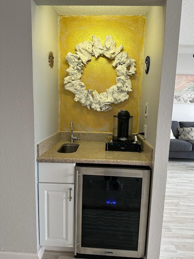 bar featuring wine cooler, light wood-type flooring, sink, and white cabinets