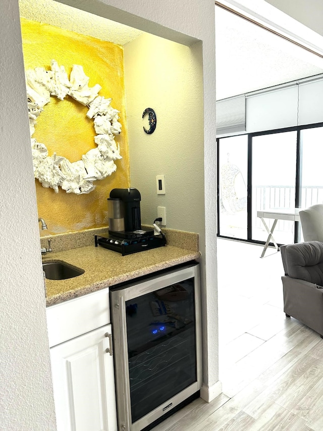 bar featuring white cabinets, light hardwood / wood-style floors, beverage cooler, and sink