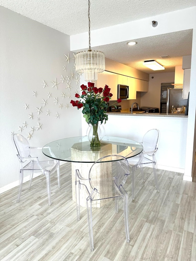 dining area with sink, an inviting chandelier, a textured ceiling, and light hardwood / wood-style floors